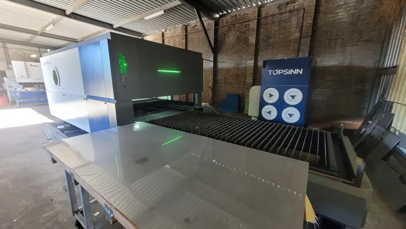 The enclosed fibre laser cutting machine in the workshop, with a polished metal sheet on the loading table in front of it